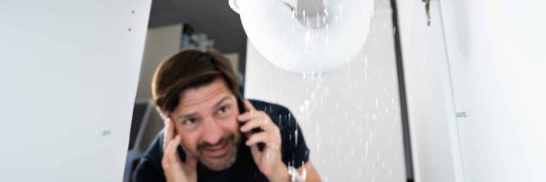A worried man finds a leaking pipe in a cabinet and calls an emergency leak plumber for help.