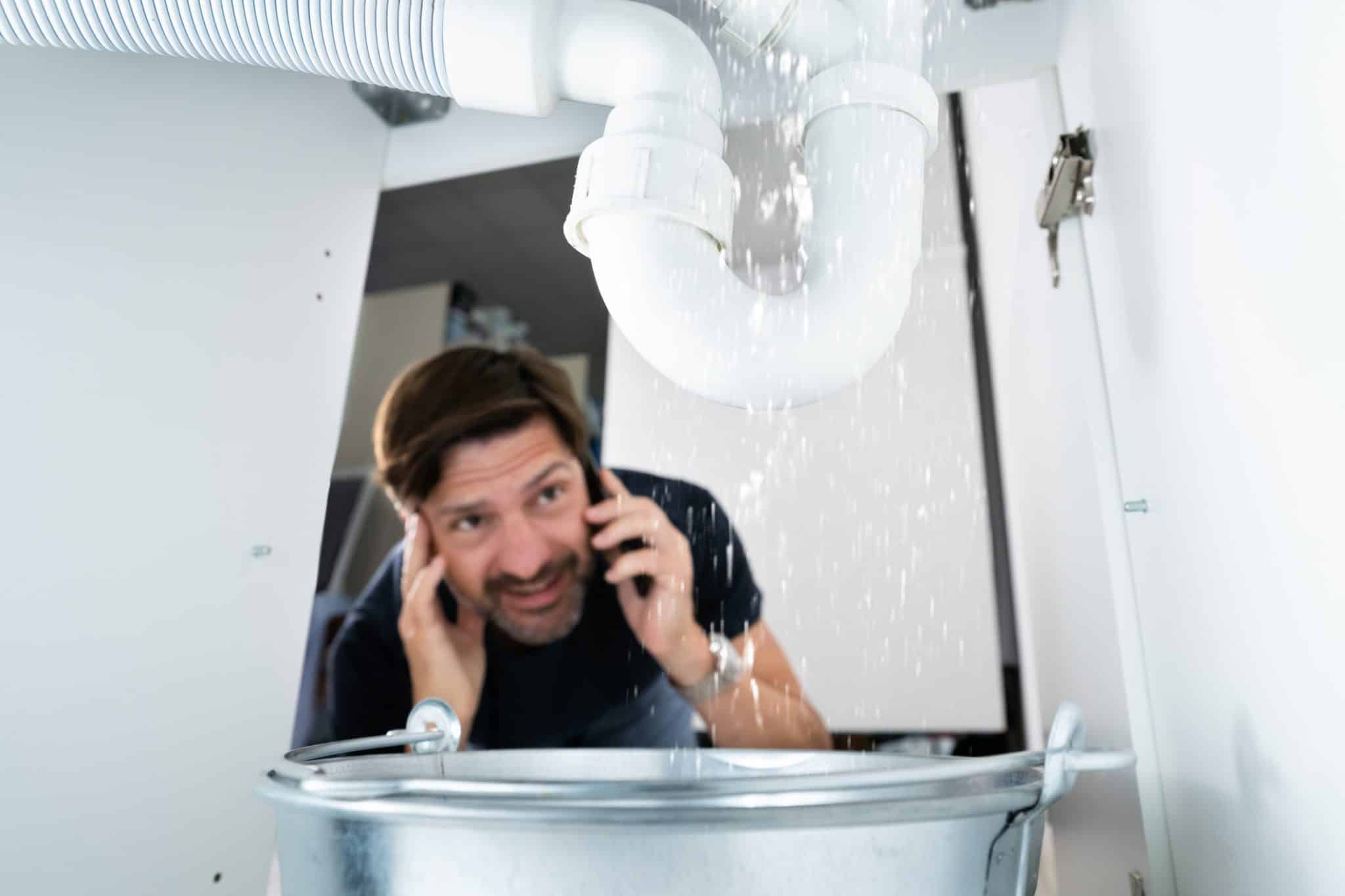 A worried man finds a leaking pipe in a cabinet and calls an emergency leak plumber for help.